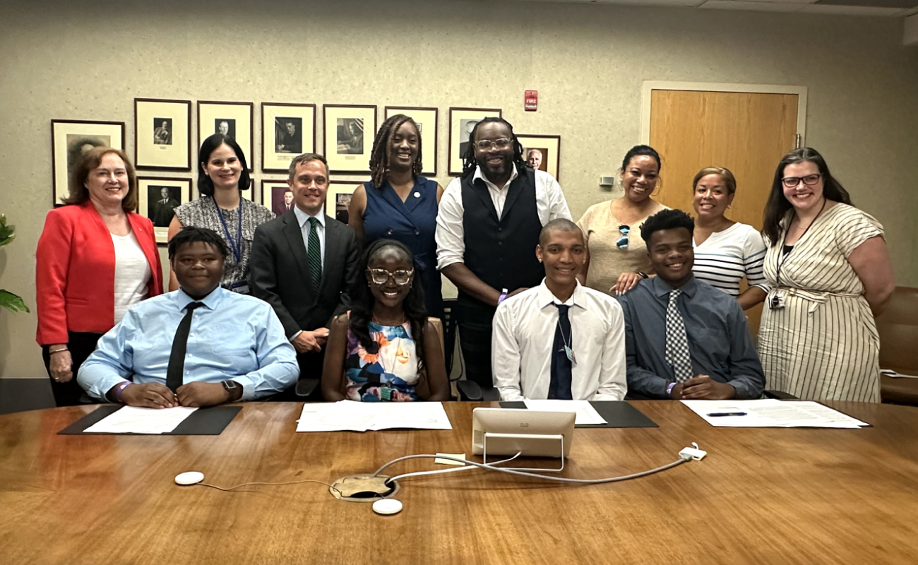 Group of people posing around a conference table with documents and a tablet.
