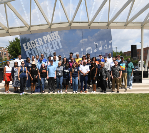 Attendees of the Eager Park concert smiling together, with the event banner in the background.