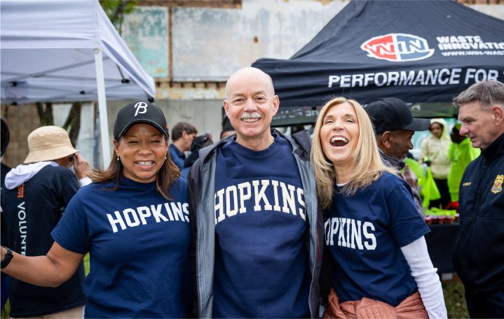 Three people smiling and standing together, wearing "HOPKINS" t-shirts at a community event.