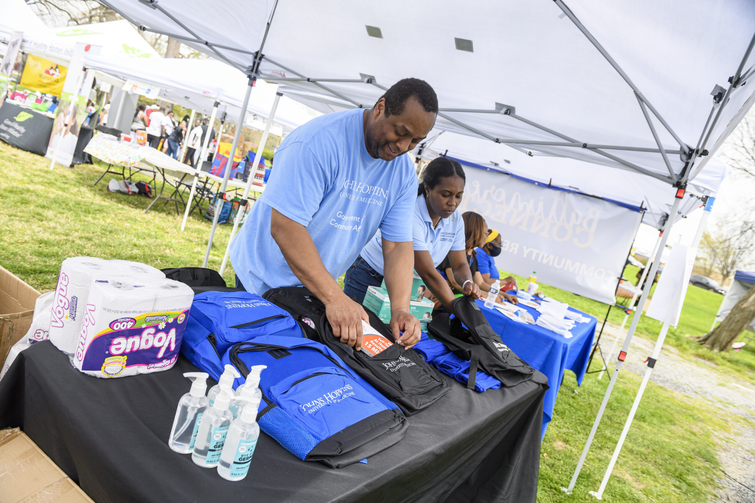 Two volunteers organize backpacks and supplies at an outdoor event table.