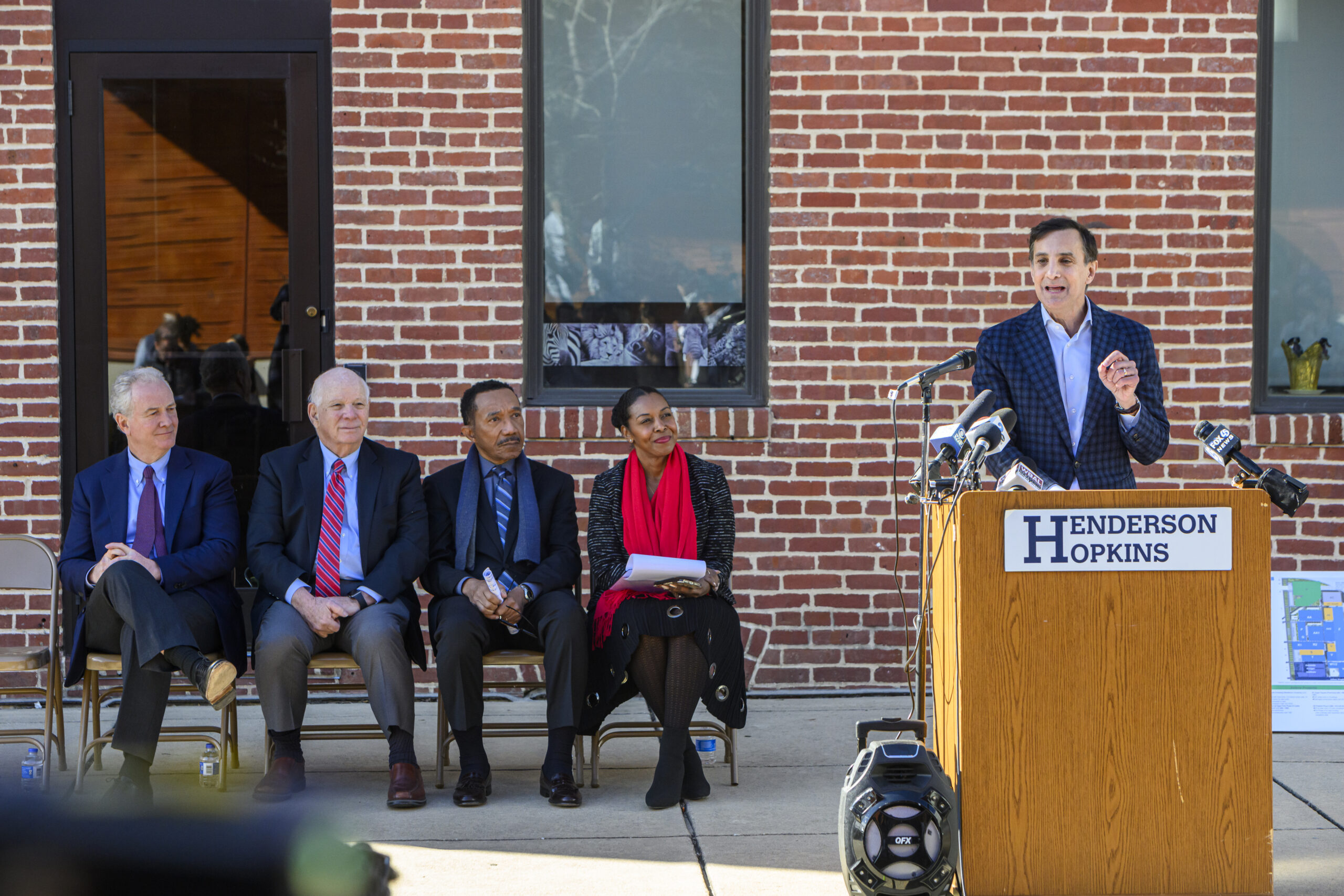 A speaker at a podium addresses an audience seated on chairs.
