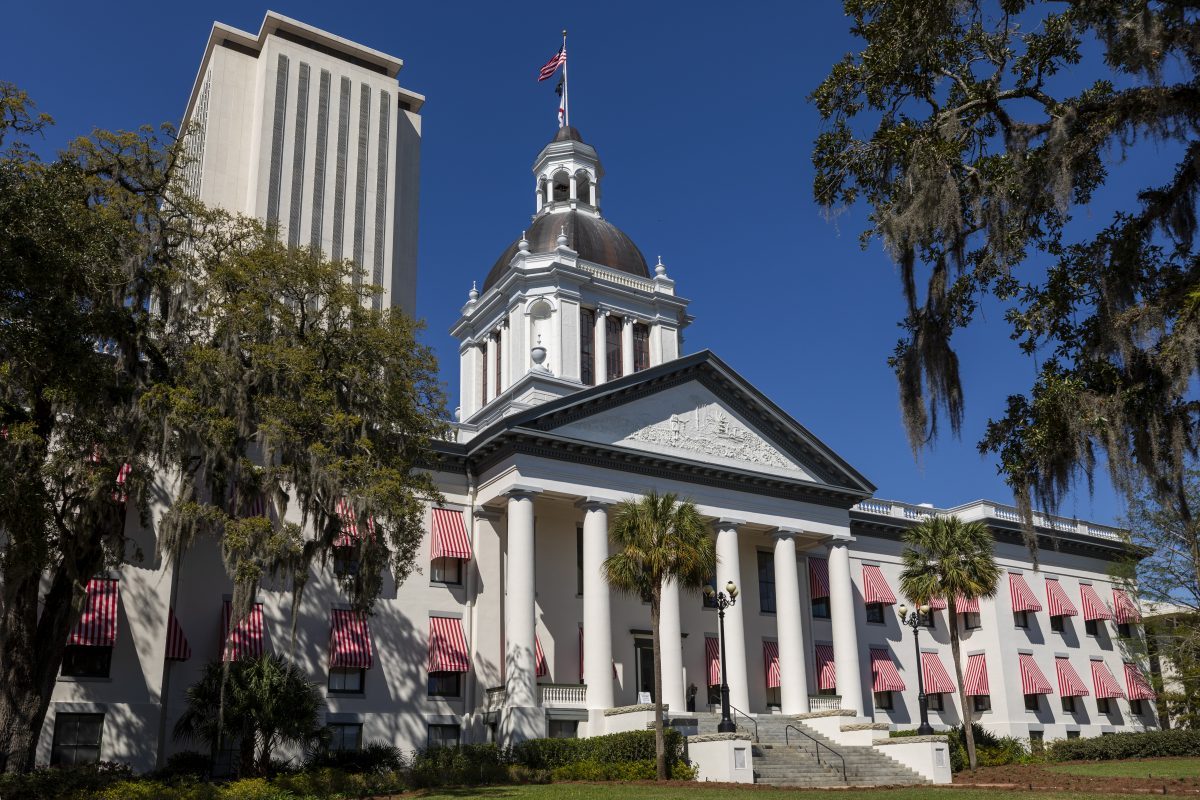 Florida State Capitol with dome, columns, and red-striped awnings under clear blue sky.