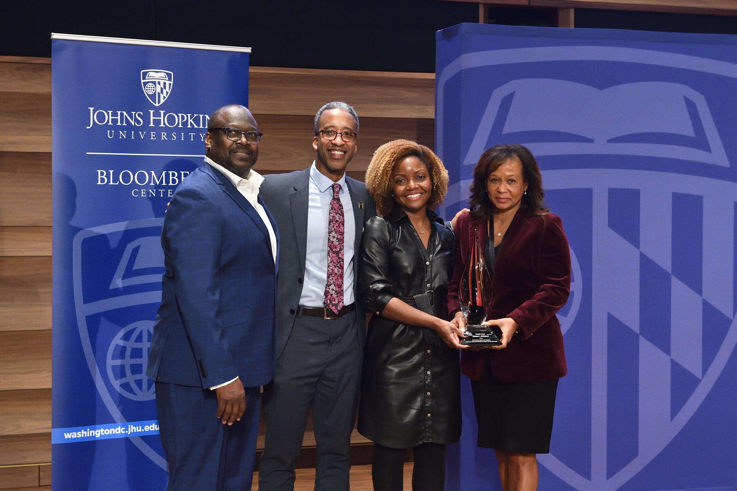 Smiling group with award in front of Johns Hopkins backdrop