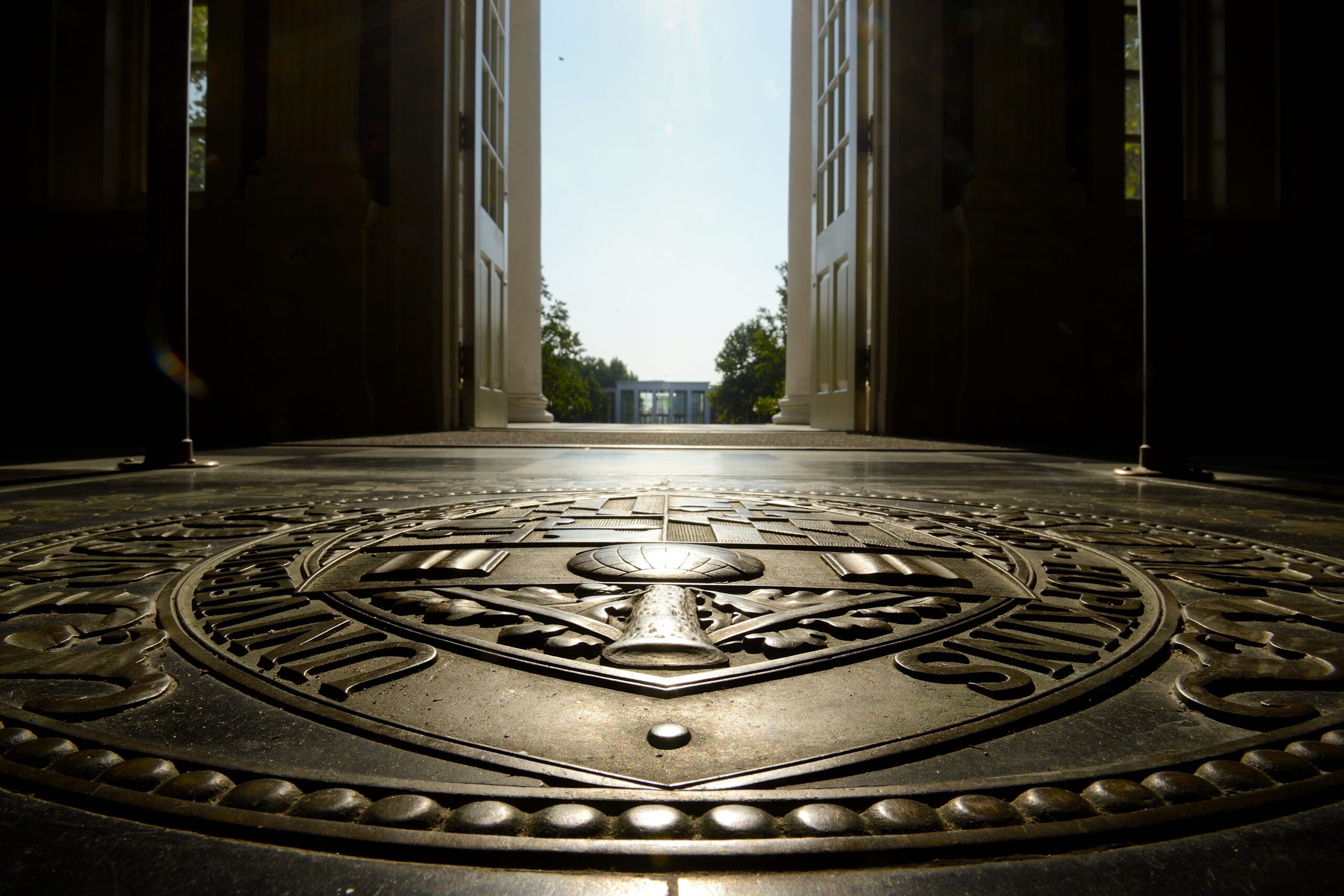 Close-up of university seal on floor with open doors and sunlight beyond