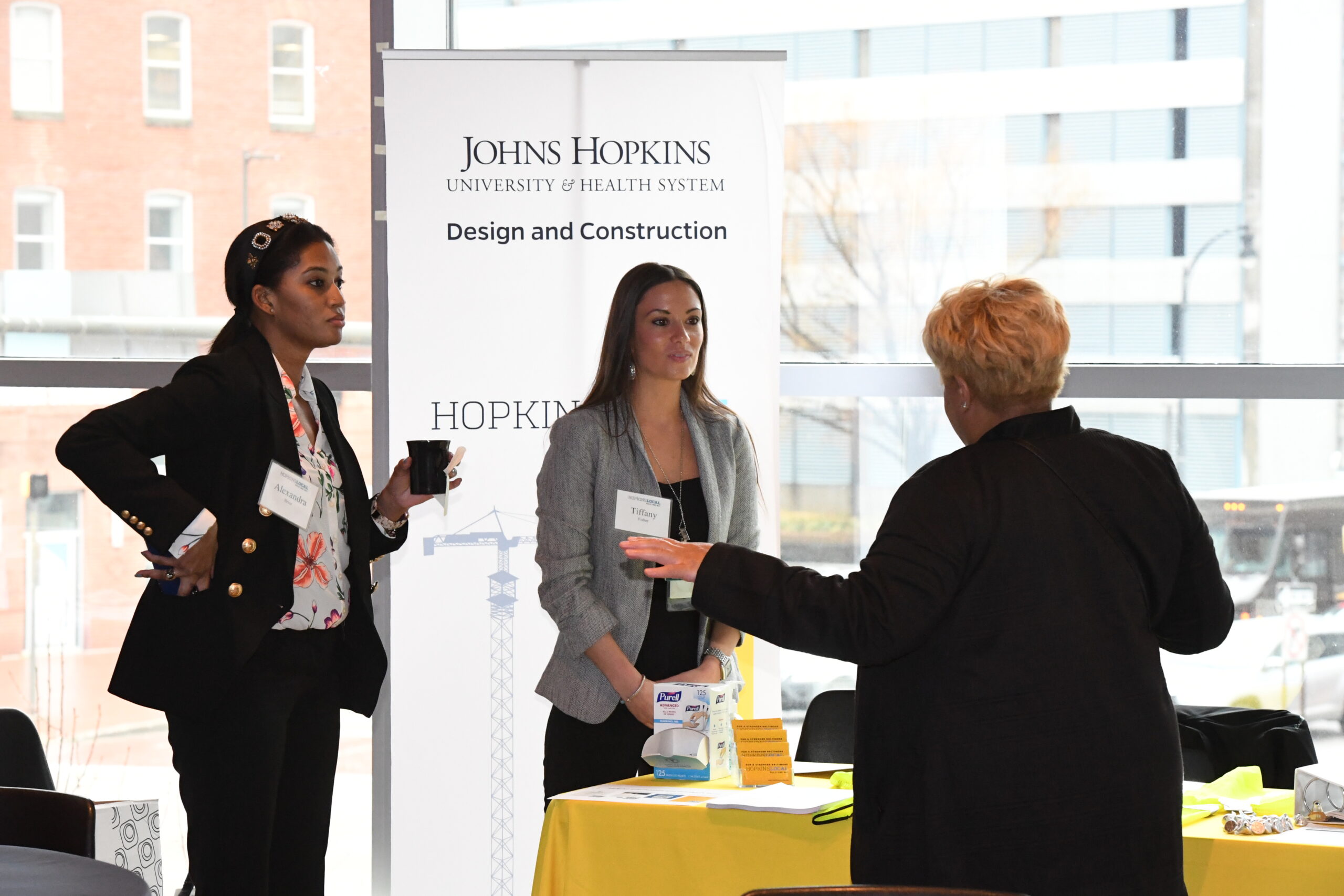 Two women engage in conversation at a table with promotional materials, featuring a Johns Hopkins banner.