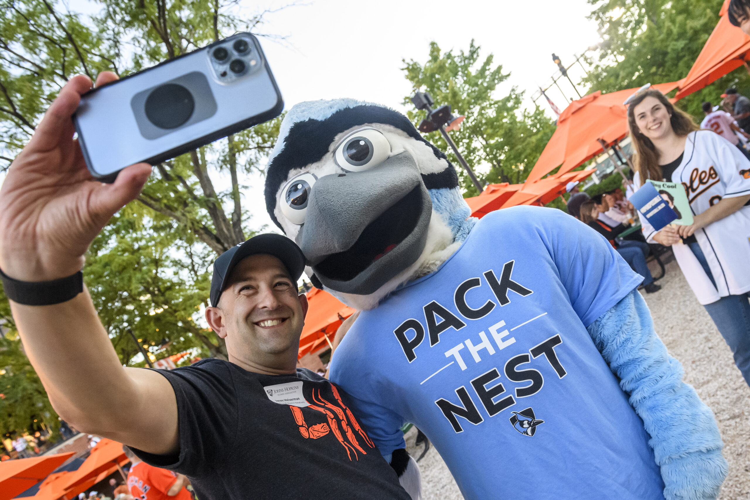 Man taking a selfie with a blue bird mascot wearing a "Pack the Nest" shirt.