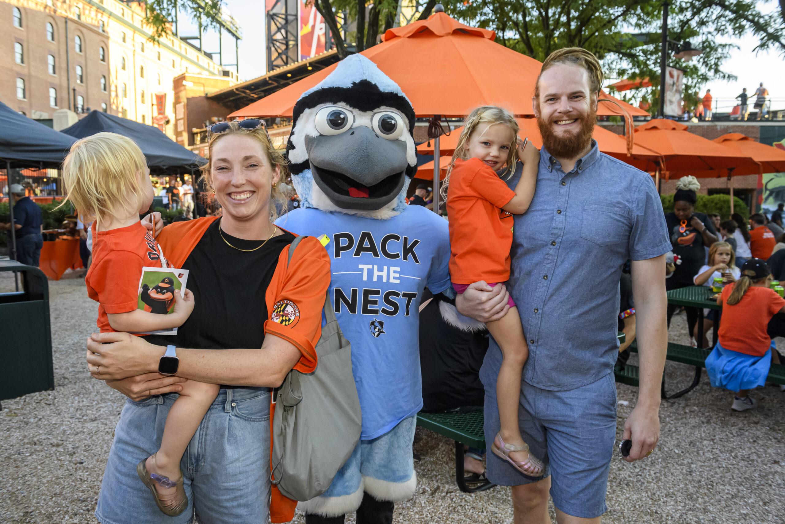 Family standing with mascot in front of vendor tents at a community event